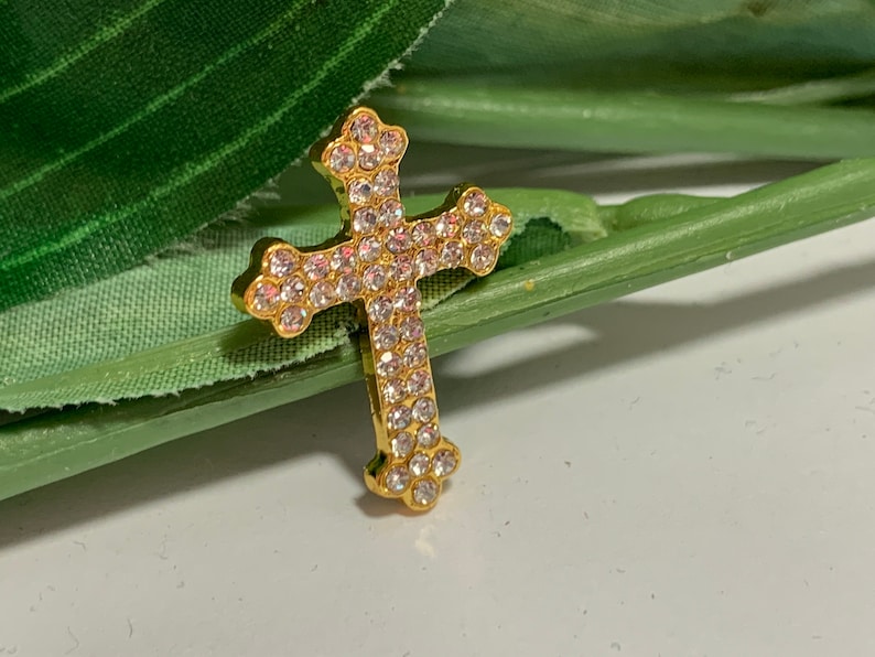 May include: A gold-toned cross pendant encrusted with clear rhinestones.