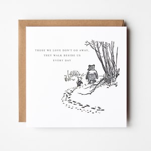Puede incluir: Tarjeta de felicitaci&oacute;n cuadrada con sobre marr&oacute;n. La tarjeta presenta una ilustraci&oacute;n en blanco y negro de Winnie the Pooh y Piglet caminando por un sendero. El texto sobre la ilustraci&oacute;n dice: "AQUELLOS QUE AMAMOS NO SE VAN, CAMINAN A NUESTRO LADO CADA D&Iacute;A."