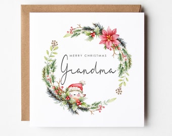 Op de afbeelding: Een witte kaart met een rode en groene aquarelkrans met een klein vogeltje dat een kerstmanmuts draagt. De tekst "Merry Christmas Grandma" is in zwarte cursieve letters geschreven.