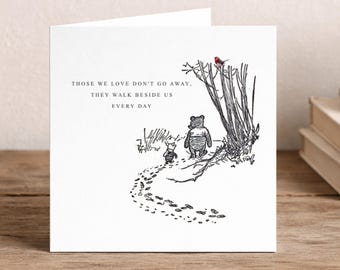 May include: A square white greeting card featuring a black ink illustration of Winnie the Pooh and Piglet walking along a path. A small red bird sits in a tree above them. The text reads: THOSE WE LOVE DON'T GO AWAY, THEY WALK BESIDE US EVERY DAY.