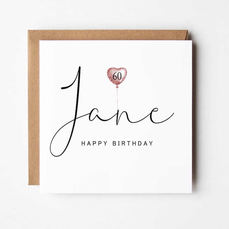 K&ouml;nnte beinhalten: Eine wei&szlig;e Karte mit einer schwarzen kursiven Schrift, die "Jane" sagt, mit einem ros&eacute;goldenen herzf&ouml;rmigen Ballon mit der Nummer "60" darauf. Der Text "Happy Birthday" steht unter dem Namen.