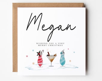May include: A white Christmas card with the name "Megan" written in black cursive script. The card has a festive illustration of three cocktails with snowflakes and the text "Wishing you a very Merry Christmas".