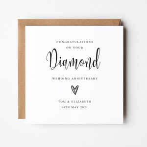 May include: A white card with black text that reads "Congratulations on your Diamond Wedding Anniversary."  A small silver heart is below the text.  The names "Tom & Elizabeth" and the date "14th May 2021" are printed below the heart.