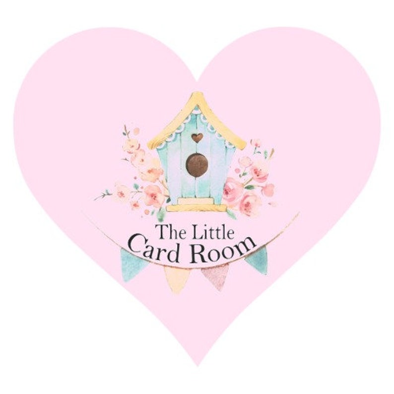 May include: A pink heart-shaped sign with a light blue birdhouse and floral accents. The sign reads "The Little Card Room".