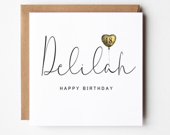May include: A white card with a black cursive font that says "Delilah Happy Birthday". A gold heart-shaped balloon with the number "18" is floating above the name.