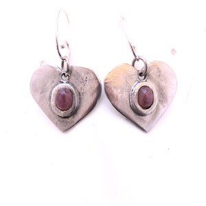 Può includere: Un paio di orecchini a forma di cuore in argento con una pietra preziosa rosa al centro di ogni cuore.