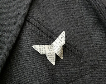 May include: A paper butterfly made from a page of a book with French text. The butterfly is sitting on a dark gray fabric.