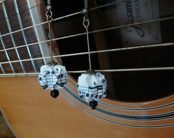 Puede incluir: Un par de pendientes con colgantes de papel origami con estampado de notas musicales blancas y negras que cuelgan de cadenas plateadas.