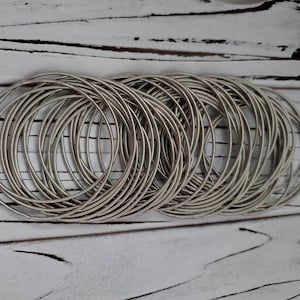 May include: A stack of silver-toned metal bangles, arranged in a circular pattern. The bangles are stacked on top of each other, creating a layered effect.