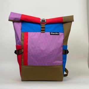 Peut inclure: Un sac à dos multicolore avec un fond brun, une section violette à motif losange, une section bleue, une section rouge et un rabat brun avec une boucle argentée. Le sac à dos a une sangle noire et une étiquette noire qui dit "flecks".