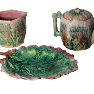 May include: A vintage tea set with a green and pink floral design. The set includes a teapot, creamer, and a leaf-shaped serving plate.