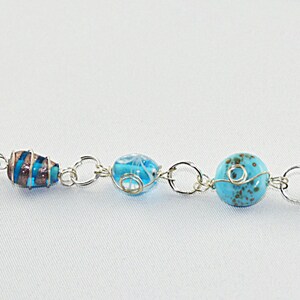 Puede incluir: Un brazalete de plata con cuentas de vidrio azul y turquesa. Las cuentas son de varias formas y tama&ntilde;os, incluyendo redondas, ovaladas y cil&iacute;ndricas.