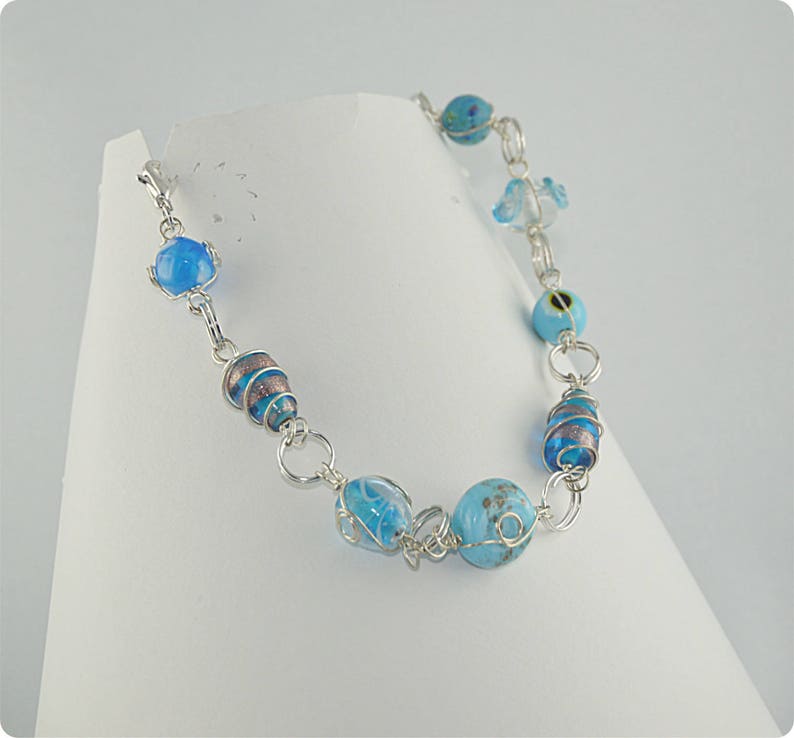Puede incluir: Un brazalete de cadena de plata con cuentas de vidrio azul y blanco. Las cuentas est&aacute;n envueltas en alambre de plata y tienen una variedad de patrones.