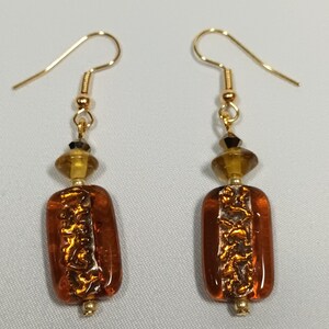 Peut inclure: Une paire de boucles d'oreilles pendantes dorées avec des perles en verre brun et des accents dorés. Les perles ont un aspect texturé et métallique.