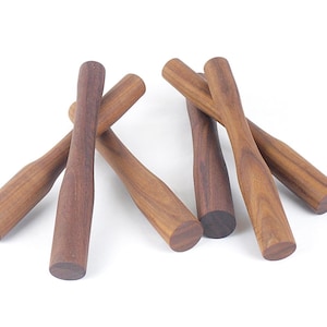 May include: Six wooden muddlers with a dark brown finish are arranged on a white background. The muddlers have a cylindrical handle that tapers to a wider, flat end. The wood grain is visible.