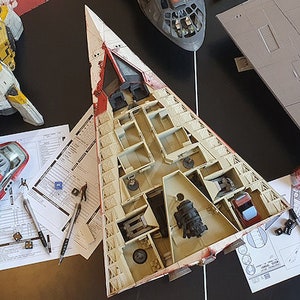 May include: A collection of model spaceships, including a white and red spaceship with an open interior, a gray spaceship, and a yellow and black spaceship. The spaceships are on a table with paper instructions and tools for building models.