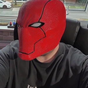 Op de afbeelding: Een felrood masker met een getextureerd oppervlak en zwarte contouren. Het masker wordt gedragen met een zwart t-shirt met de tekst "Los Angeles" in een gestileerd lettertype.