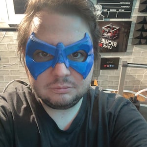 May include: A bright blue, rigid, molded plastic eye mask featuring a pointed, angular design that covers the eye area and bridge of the nose. The mask has a smooth, slightly reflective finish and cutouts for the eyes, secured by a strap.
