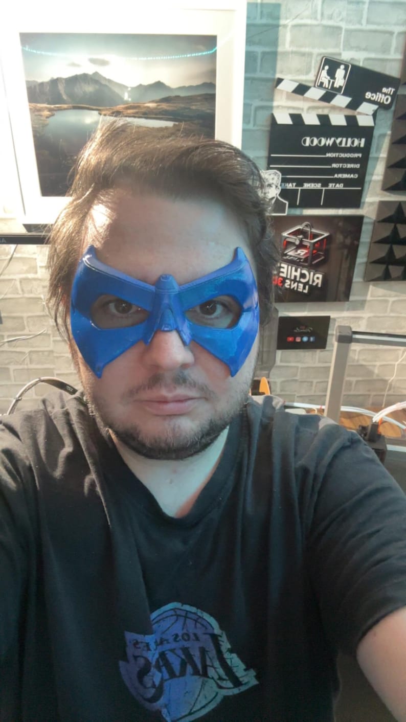 May include: A bright blue, rigid, molded plastic eye mask featuring a pointed, angular design that covers the eye area and bridge of the nose. The mask has a smooth, slightly reflective finish and cutouts for the eyes, secured by a strap.