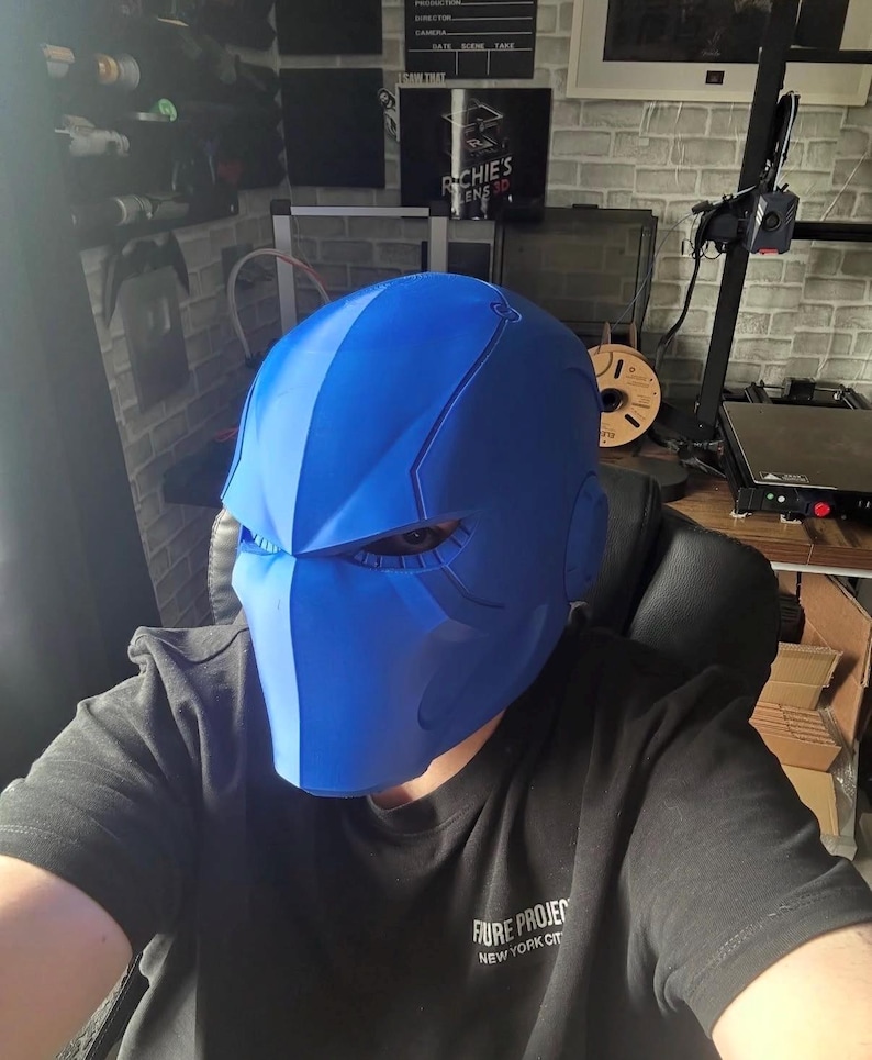 May include: A striking blue helmet with a modern, angular design. The helmet has a central stripe and side features, possibly for a futuristic or superhero aesthetic. The wearer is wearing a black t-shirt with the text "FUTURE PROJECT NEW YORK CITY".