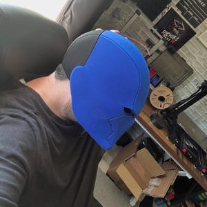 Op de afbeelding: Een blauw en zwart masker met een getextureerd oppervlak. Het masker is felblauw aan de voorkant en zwart aan de bovenkant. Het masker is waarschijnlijk een kostuum- of cosplay-item.