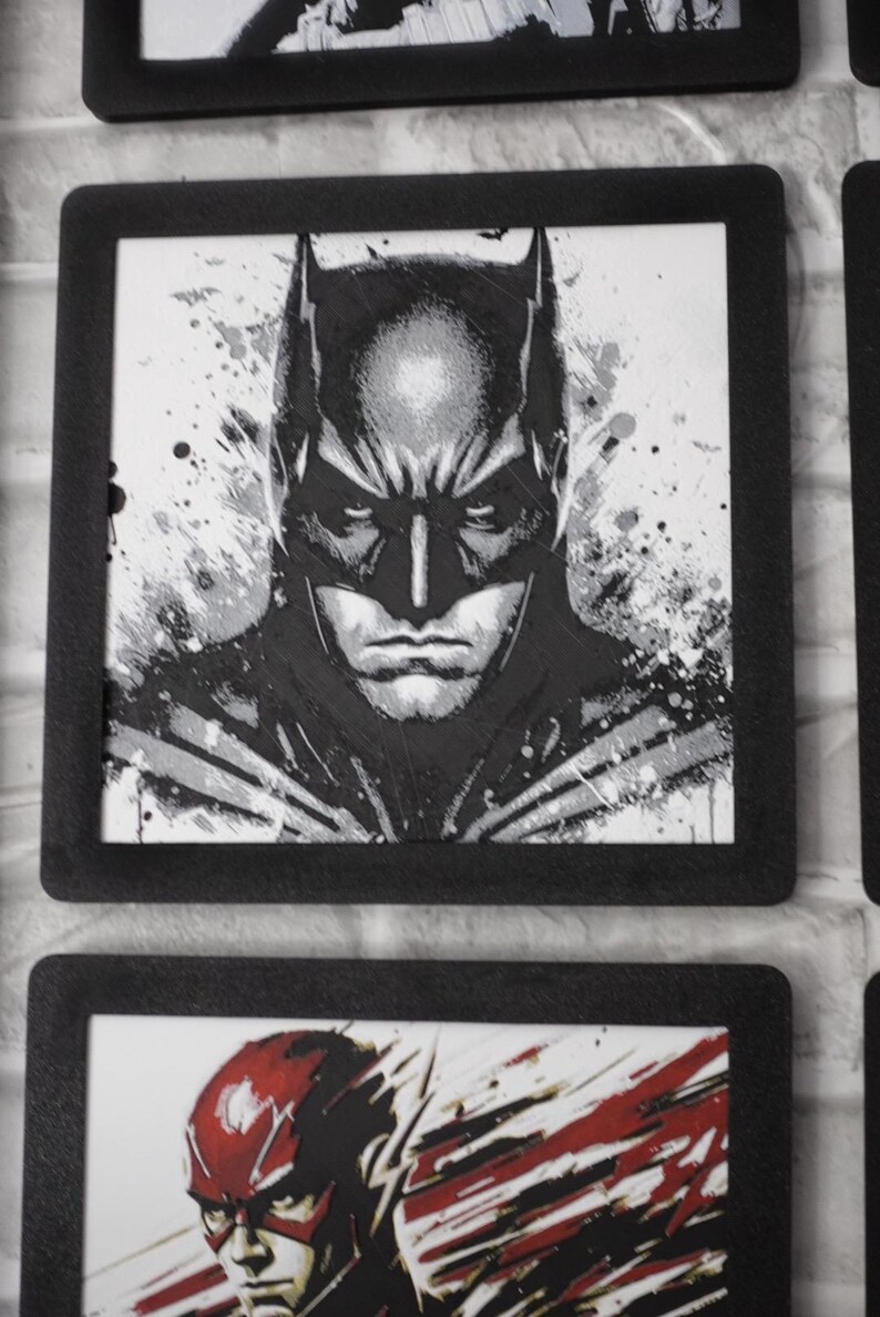 May include: A square black-framed wall art piece featuring a black and white ink-style illustration of Batman. The character is depicted from the chest up with a focused expression, surrounded by abstract paint splatters and textured brush strokes.