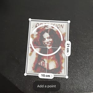 May include: A rectangular print featuring a portrait of a person with dark hair and a smiling expression, surrounded by red and orange abstract watercolor-style splashes. The word OBSESSION is printed at the top. It measures 15 cm by 21 cm.