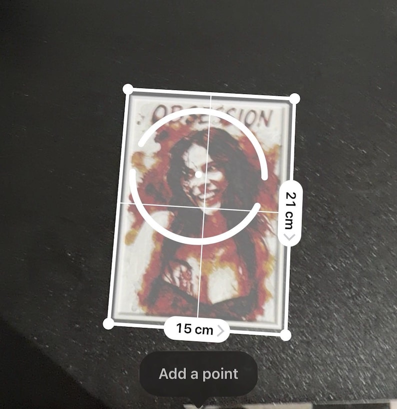 May include: A rectangular print featuring a portrait of a person with dark hair and a smiling expression, surrounded by red and orange abstract watercolor-style splashes. The word OBSESSION is printed at the top. It measures 15 cm by 21 cm.