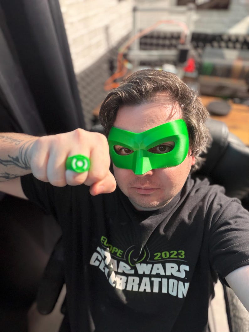 Puede incluir: Una persona con una m&aacute;scara verde y un anillo verde. La persona lleva una camiseta negra con el texto "ELOP 2023 STAR WARS CELEBRATION". El fondo est&aacute; borroso, con enfoque en la persona y los accesorios.