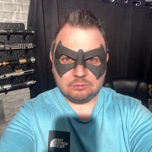 May include: A matte black, rigid eye mask featuring a pointed, angular design that covers the area around the eyes and the bridge of the nose. The mask has two large, contoured eye openings and a smooth, solid surface texture.