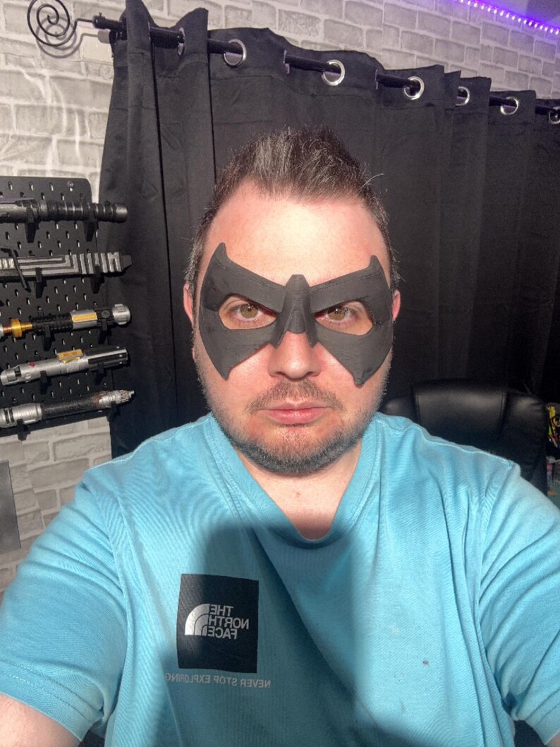May include: A matte black, rigid eye mask featuring a pointed, angular design that covers the area around the eyes and the bridge of the nose. The mask has two large, contoured eye openings and a smooth, solid surface texture.