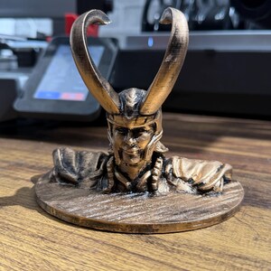 May include: A bronze-colored figurine of a horned character, possibly a mythological figure or a character from a fantasy story. The figurine is on a round base and has intricate details.