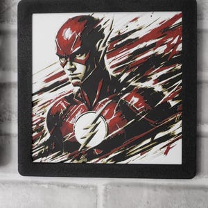May include: A square framed wall art piece featuring a stylized illustration of The Flash in a red and black suit with a white lightning bolt emblem on the chest. The artwork uses dynamic, streaking brushstroke effects in red, black, and white.