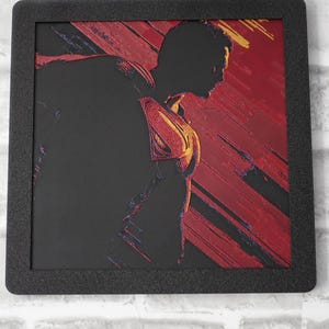 May include: A square framed wall art piece featuring a black silhouette of Superman in profile against a textured red and black background. The iconic S-shield emblem on the chest is highlighted in yellow and red, with diagonal brushstroke textures.