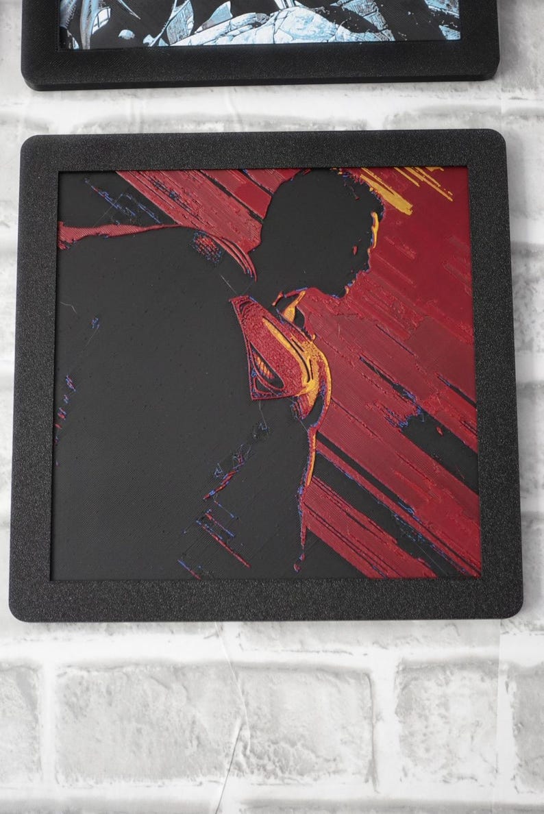 May include: A square framed wall art piece featuring a black silhouette of Superman in profile against a textured red and black background. The iconic S-shield emblem on the chest is highlighted in yellow and red, with diagonal brushstroke textures.