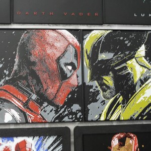 May include: Two rectangular framed wall art pieces featuring stylized graphic illustrations. The left piece depicts a red and black masked character in profile, while the right piece shows a yellow and black masked character in profile.
