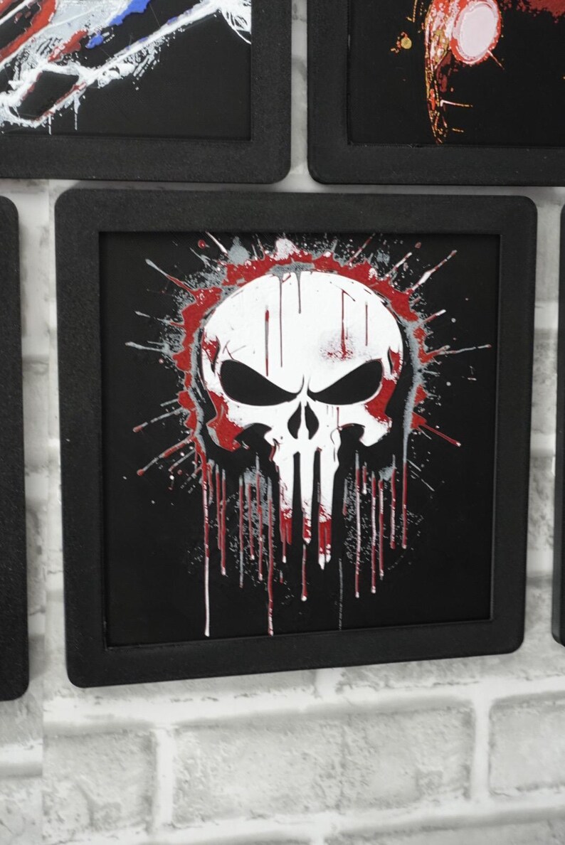 May include: A square black frame containing a graphic print of a white skull with black eye sockets and nose cavity. The design features red and grey paint splatter effects that drip downwards over a solid black background within the frame.