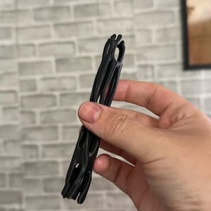 May include: A black, elongated, cylindrical object with a hollow, cage-like structure featuring multiple vertical slats and open spaces throughout its length, designed with a textured, organic appearance and a smooth, matte finish.