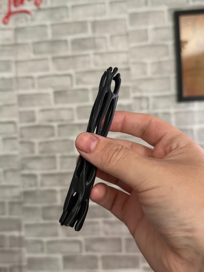 May include: A black, elongated, cylindrical object with a hollow, cage-like structure featuring multiple vertical slats and open spaces throughout its length, designed with a textured, organic appearance and a smooth, matte finish.