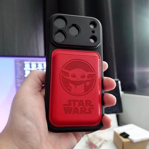 May include: Black phone case with a red magnetic card holder featuring a Baby Yoda design and the Star Wars logo. The case has a black camera module with three lenses.