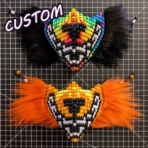 May include: Two handmade beaded masks crafted from colorful plastic pony beads. The top mask features a rainbow pattern with black faux fur side accents. The bottom mask displays an orange and yellow design with orange faux fur side accents.