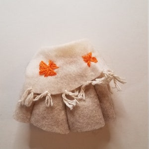May include: A white felt skirt with orange embroidered flowers and white fringe around the bottom.