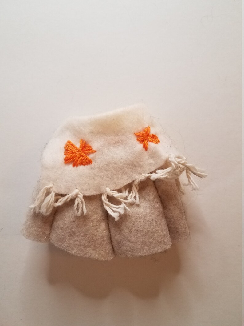 May include: A white felt skirt with orange embroidered flowers and white fringe around the bottom.