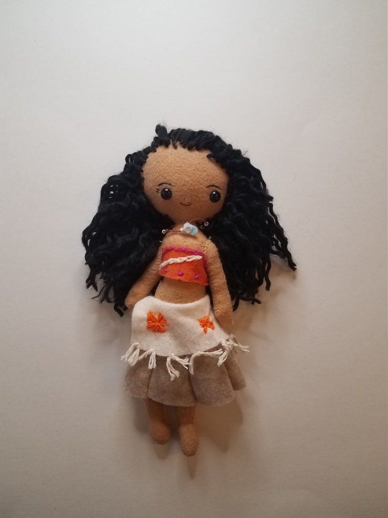 May include: Handmade felt doll with long black curly hair, wearing an orange and white top and a brown skirt with orange flowers.