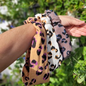 May include: Three leopard print headbands in different colours: brown with purple spots, white with black spots, and grey with blue spots.
