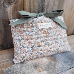 Può includere: Un astuccio trapuntato floreale con un fiocco verde salvia. L'astuccio presenta un motivo di piccoli fiori color pesca e bianchi con foglie verdi su sfondo crema. L'etichetta recita "L&A CREATION - HANDMADE".