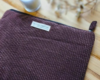 Puede incluir: Un estuche rectangular de pana marrón oscuro con cremallera y una etiqueta de tela blanca cosida en la parte frontal. La etiqueta muestra el texto L&A CREATION y una dirección web en tinta negra. El estuche tiene un tirador a juego.