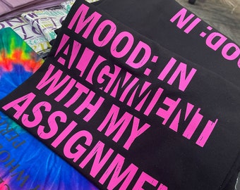May include: Black t-shirt with pink text that reads "MOOD: IN ALIGNMENT WITH MY ASSIGNMENT".