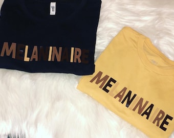 May include: Two t-shirts with the word "MELANINAIRE" printed on them in black and brown letters. The shirts are navy blue and yellow.