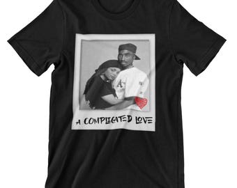 May include: Black and white photograph of a couple embracing. The man is wearing a baseball cap and the woman is wearing a long-sleeved shirt. The photo is in a white frame with the text "A complicated love" printed below it.